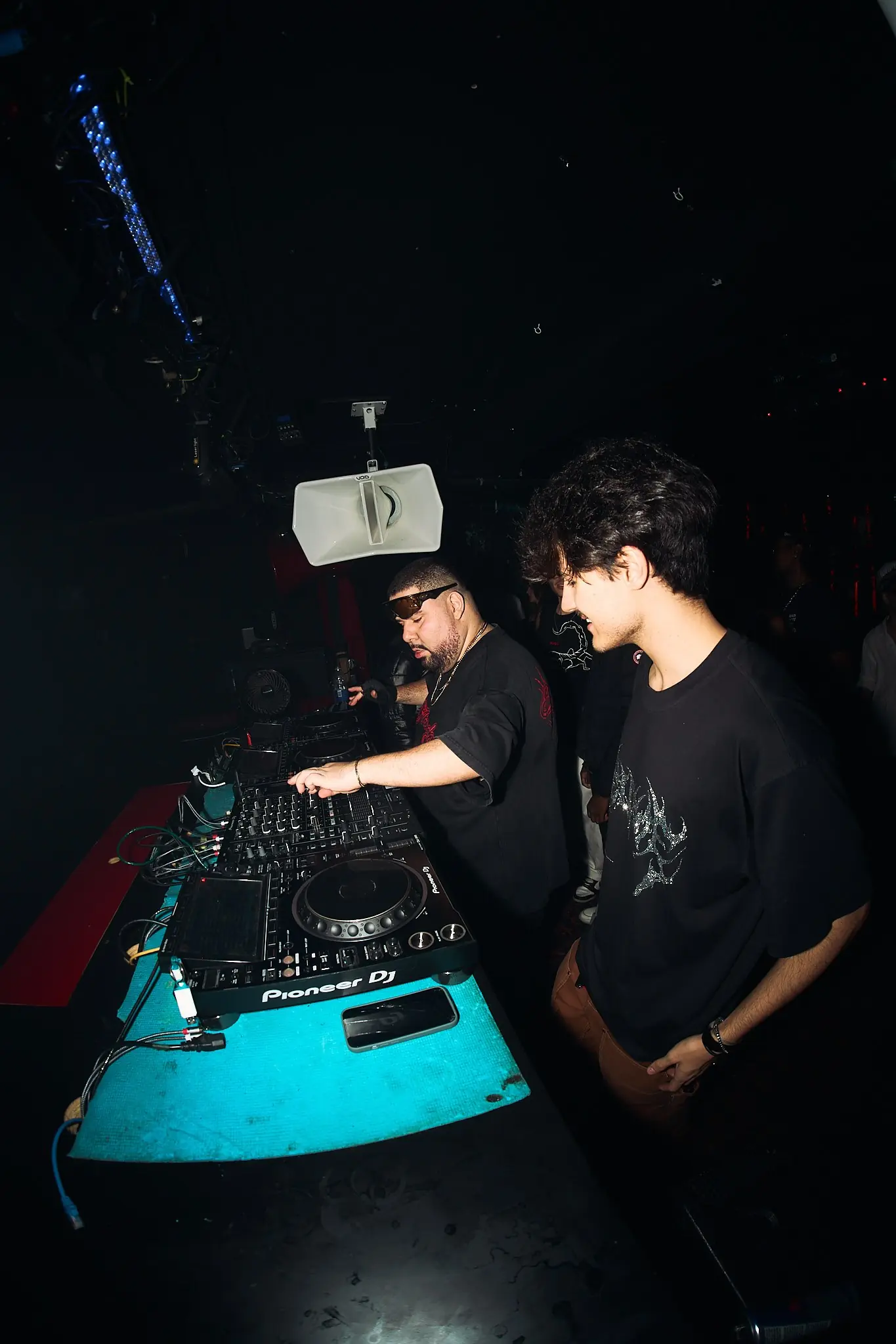 Dorom ao lado de outro DJ na cabine, sob luz baixa